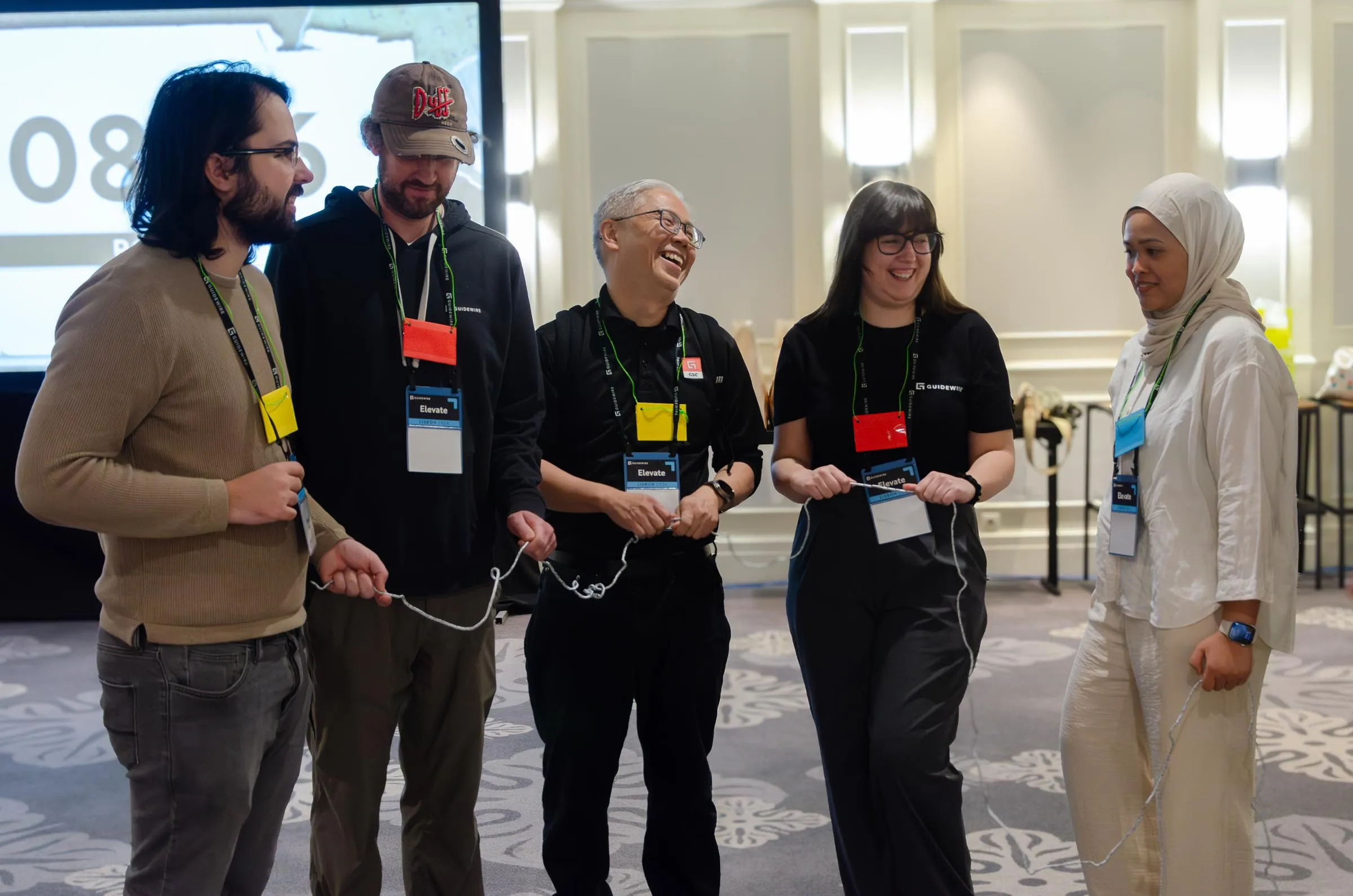 A playful moment at an event, five people gathered around one rope, laughing